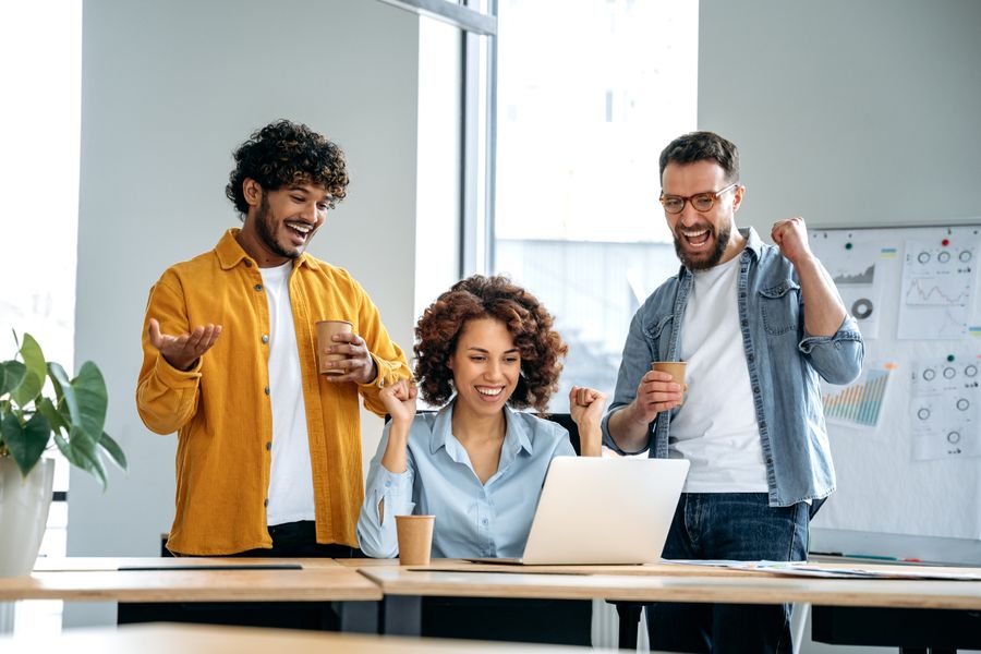 Two men and a women looking at a laptop and celebrating in an office